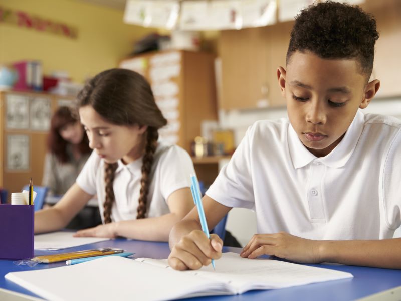 Primary age boy and girl writing at a table